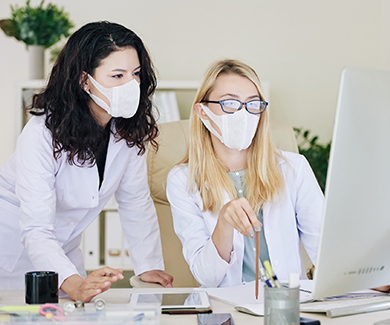 Two masked medical staff look at a computer screen